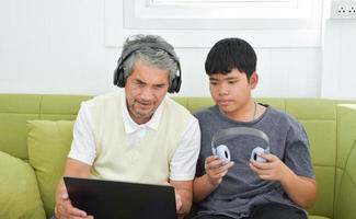 vovô sênior asiático e seu filho estão passando momentos juntos em casa para conectar o fone de ouvido com seu laptop para assistir e jogar jogos online, foco suave e seletivo, elevando o conceito de adolescentes. foto