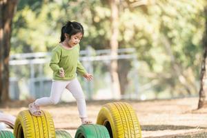 sorriso de linda garota asiática brinca na escola ou jardim de infância ou playground. atividade de verão saudável para crianças. menina asiática escalando ao ar livre no playground. criança brincando no playground ao ar livre. foto