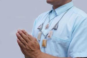 homem de camisa azul, usa amuleto de buda, rezando com as mãos gesto de oração budista. wai na cultura tailandesa. conceito, wearship para sorte, fé e crença. padrão de respeito e saudação. foto