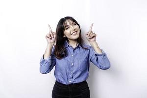 mulher asiática animada vestindo camisa azul apontando para o espaço da cópia em cima dela, isolado pelo fundo branco foto