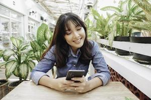 uma mulher asiática feliz em um restaurante, vestindo uma camisa azul e segurando seu telefone foto