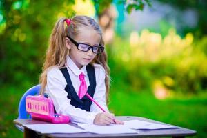 adorável menina da escola na mesa com notas e lápis ao ar livre. de volta à escola. foto