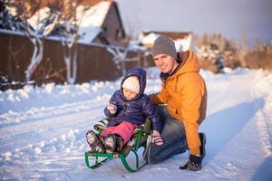 jovem pai andando de trenó com sua filhinha adorável em um dia ensolarado de inverno foto