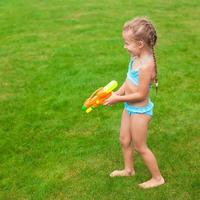 menina adorável brincando com pistola de água ao ar livre em dia ensolarado de verão foto