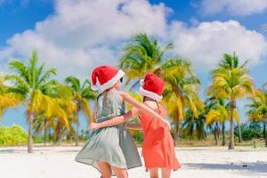 meninas adoráveis em chapéus de Papai Noel durante as férias na praia se divertem juntos foto