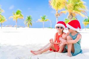 meninas adoráveis em chapéus de Papai Noel durante as férias na praia se divertem juntos foto