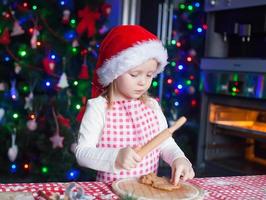 adorável menina de chapéu de Papai Noel assando biscoitos de gengibre em casa foto
