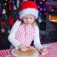 menina adorável com rolo assando biscoitos de gengibre para o natal foto