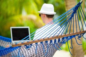 jovem com laptop na rede em férias tropicais foto