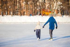 menina adorável com pai aprendendo a patinar na pista de gelo foto