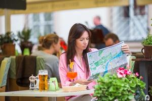 linda mulher sentada em um café ao ar livre com mapa. turista feliz aproveita as férias europeias no restaurante openair foto