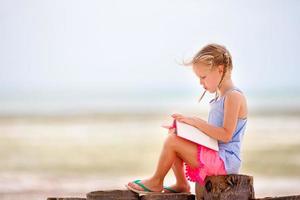 menina adorável lendo livro durante praia branca tropical foto