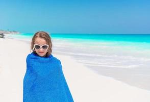 menina se divertindo correndo com a toalha e aproveitando as férias na praia tropical com areia branca e água do mar turquesa foto