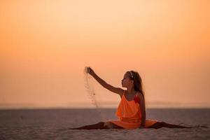 silhueta de menina adorável na praia branca ao pôr do sol foto