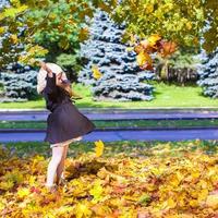 menina engraçada joga folhas de outono no parque em um dia ensolarado de outono