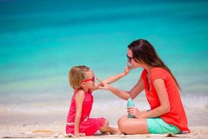 mãe aplicando creme de proteção solar para sua filha na praia tropical foto