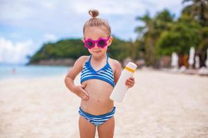 menina adorável em traje de banho esfrega protetor solar ela mesma foto