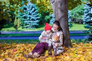 moda jovem mãe e sua adorável filha sentada perto de big maple em lindo dia de outono foto