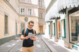 homem turista com um mapa da cidade e mochila na rua da europa. menino caucasiano olhando com mapa da cidade europeia. foto