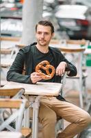 belo jovem segurando pretzel e relaxando no parque foto