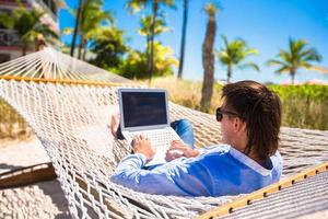 jovem trabalhando com laptop na rede durante as férias na praia foto