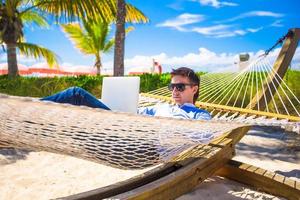 jovem trabalhando no laptop em rede na praia tropical foto