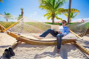 jovem trabalhando com laptop na rede durante as férias na praia foto