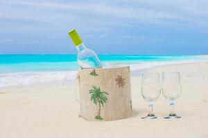 garrafa de vinho branco e dois copos na praia exótica foto