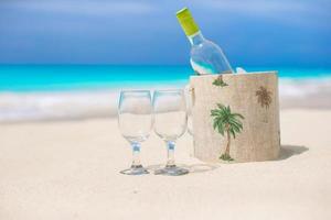 garrafa de vinho branco e dois copos na praia exótica foto