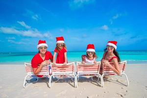 família de chapéu de Papai Noel se divertindo na praia tropical foto