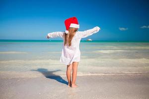 vista traseira da menina bonitinha de chapéu vermelho papai noel na praia foto