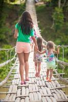 visão traseira da jovem mãe com suas filhas na ponte pênsil sobre o rio loboc, filipinas foto