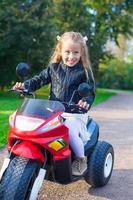 adorável menina feliz na jaqueta de couro sentada em sua motocicleta de brinquedo foto