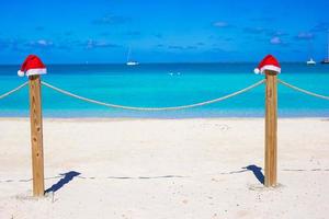 dois chapéus de papai noel vermelhos na cerca na praia branca tropical foto