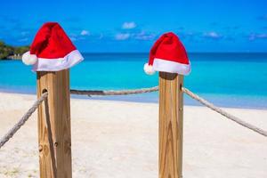 dois chapéus de papai noel vermelhos na cerca na praia branca tropical foto