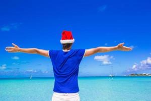 vista traseira do jovem com chapéu de Papai Noel na praia tropical foto