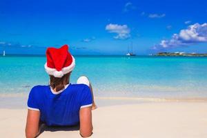 vista traseira do jovem com chapéu de Papai Noel na praia tropical foto