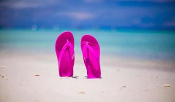 chinelos de praia vibrante rosa na areia branca no fundo do mar foto