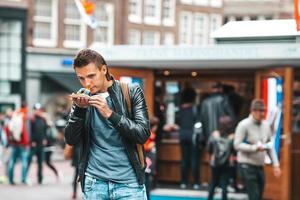 Feliz turista caucasiano com arenque fresco com cebola e bandeira da Holanda em Amsterdã. comida tradicional holandesa ao ar livre foto