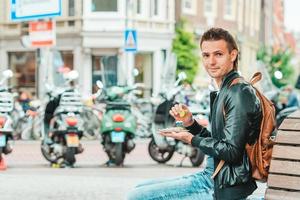 Feliz turista caucasiano com arenque fresco com cebola e bandeira da Holanda em Amsterdã. comida tradicional holandesa ao ar livre foto