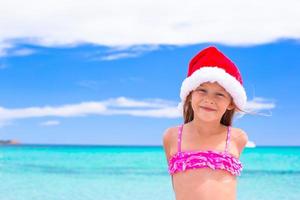 menina adorável com chapéu de Papai Noel vermelho na praia tropical foto