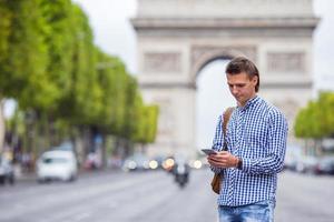 jovem homem caucasiano segurando um telefone na champs elysees em paris foto