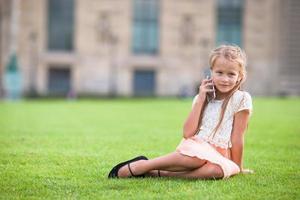 menina adorável criança com telefone em paris durante as férias de verão foto