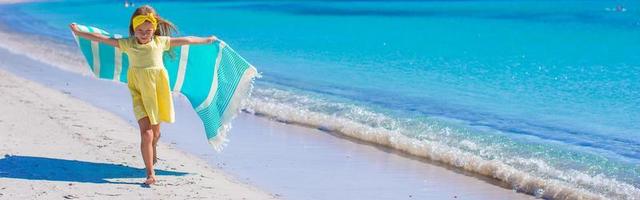 menina se divertir com toalha de praia durante as férias tropicais foto