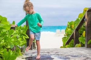 menina bonitinha lava a areia de seus pés na praia tropical foto