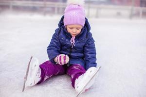 adorável menina sentada no gelo com patins após a queda foto