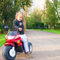 menina adorável do rock na jaqueta de couro sentada em sua motocicleta de brinquedo foto