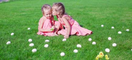 irmã mais velha beijando mais jovem em uma clareira verde de ovos de páscoa foto