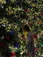 jovem no fundo da árvore de natal em miami. linda árvore de natal na área popular na véspera de natal e luzes foto