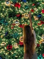jovem no fundo da árvore de natal em miami. linda árvore de natal na área popular na véspera de natal e luzes foto